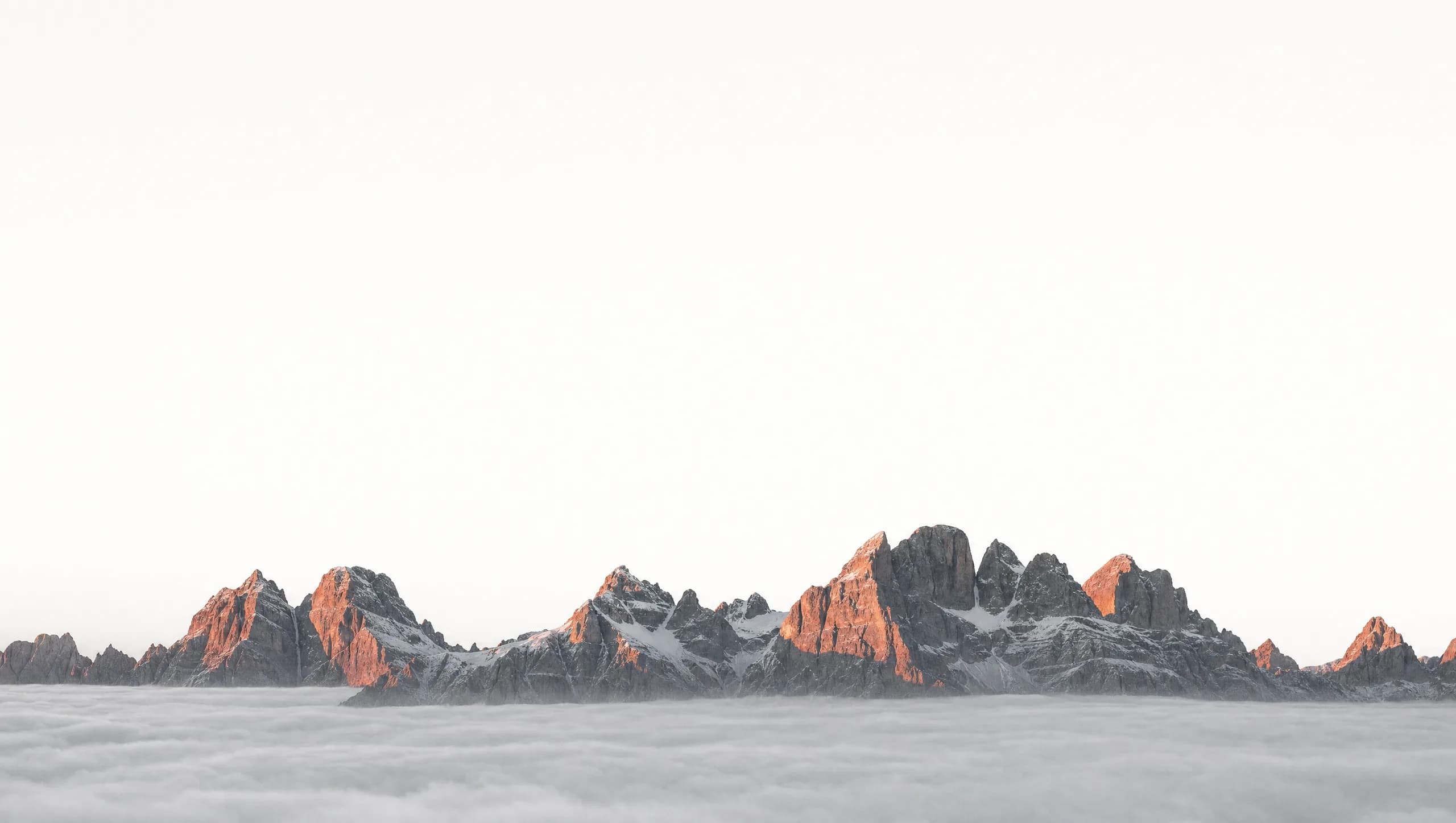 An immense mountain range breaking through a flat sea of cloud at first light